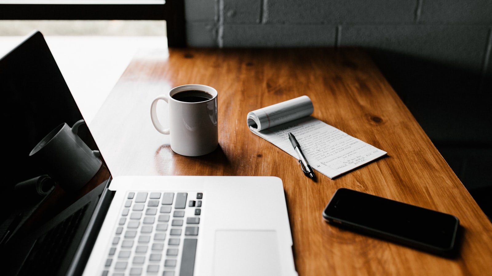 Portátil, libreta y taza sobre una mesa de trabajo de madera